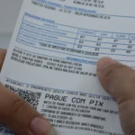 Mãos seguram conta de água com detalhes de análise de qualidade e instruções para pagamento via Pix