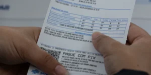 Mãos seguram conta de água com detalhes de análise de qualidade e instruções para pagamento via Pix
