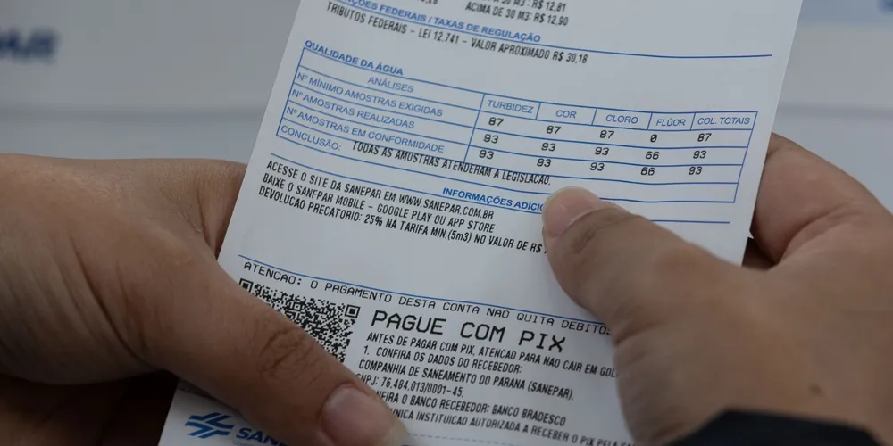 Mãos seguram conta de água com detalhes de análise de qualidade e instruções para pagamento via Pix