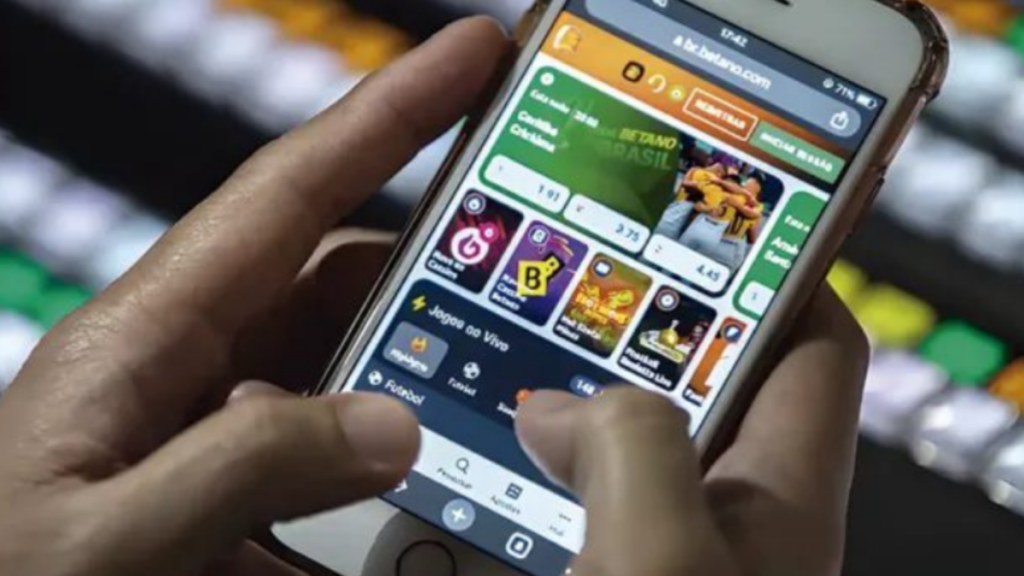 Um homem opera um smartphone com aplicativo de apostas esportivas na tela