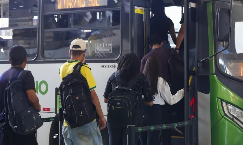 Um grupo de pessoas entra em um ônibus em uma parada urbana
