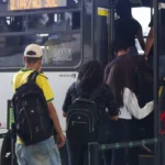Um grupo de pessoas entra em um ônibus em uma parada urbana