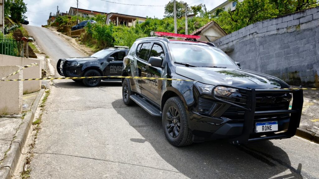 Dois veículos de segurança bloqueiam uma rua residencial com fita de isolamento