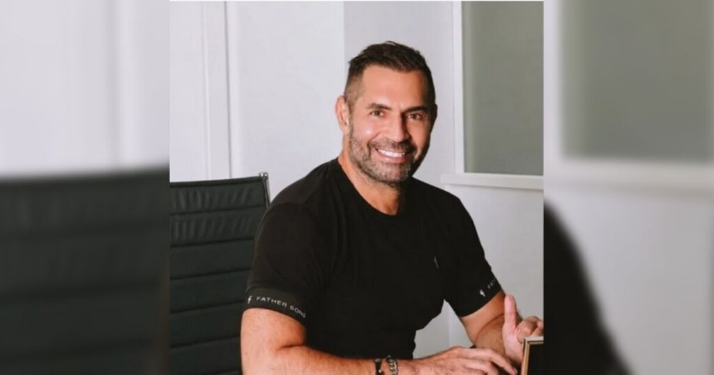 Um homem de camiseta preta sentado em uma cadeira em um ambiente interno