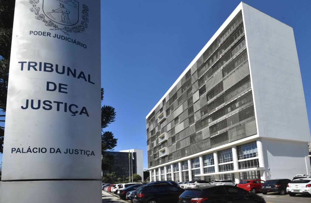 Um prédio de múltiplos andares com fachada de vidro e uma placa com inscrição de tribunal ao lado de carros estacionados