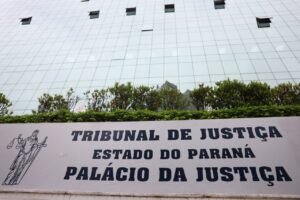 Um prédio de vidro com uma placa indicando o Tribunal de Justiça do Estado do Paraná e o Palácio da Justiça