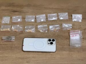 Várias porções de substâncias em sacos plásticos dispostas sobre uma superfície de madeira ao lado de um celular
