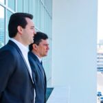 Dois homens de terno observam uma via urbana de um terraço com vista para edifícios
