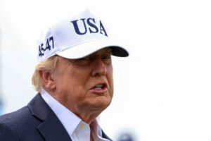 Um homem de terno e camisa branca usa boné branco com as letras USA e números 45-47