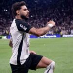 Um jogador comemora no gramado de um estádio lotado durante partida noturna